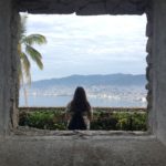 zdjęcie dziewczyny siedzącej tyłem w tle panorama morza i miasta i palmy