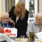 zdjęcie trzech starszych panów siedzących przy stole i starsza Pani stojąca za jednym z nich