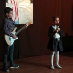chłopiec z gitarą na scenie, dziewczynka przy mikrofonie śpiewa