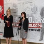 dwie kobiety przy mikrofonach, przemawiające do publiczności, w tle baner 100. rocznicy powstania wielkopolskiego